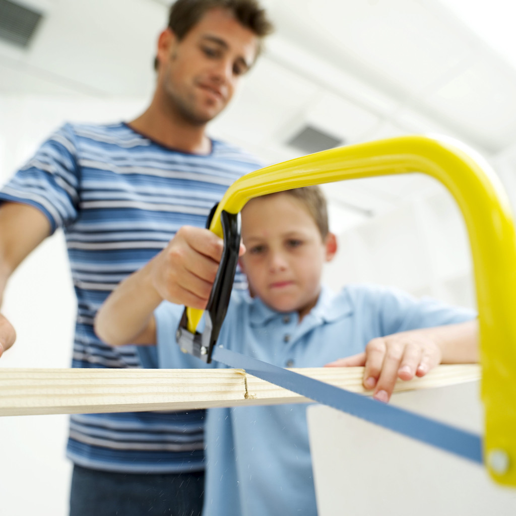Boy Sawing Piece of Wood in Half with His Father